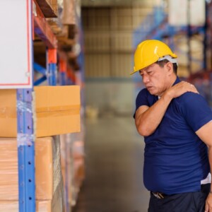 A warehouse worker holding his neck and shoulder in pain
